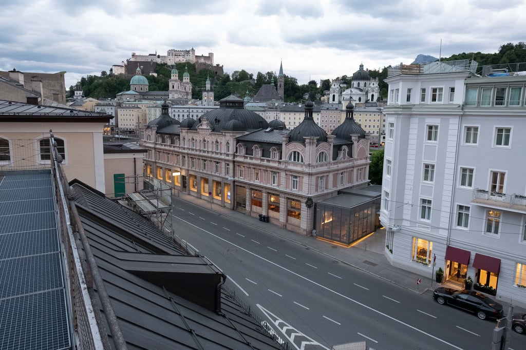 The salmon-pink Cafe Bazar building with its row of small onion-dome cupolas on Schwarzstrasse with the Salzburg fortress and old town silhouette behind