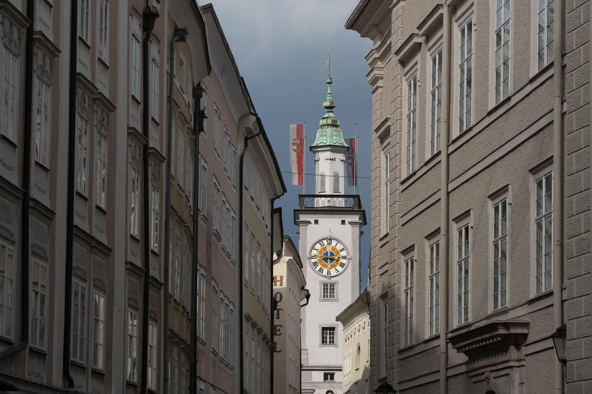Old town hall tower with clock face seen between narrow old-town facades in Salzburg.