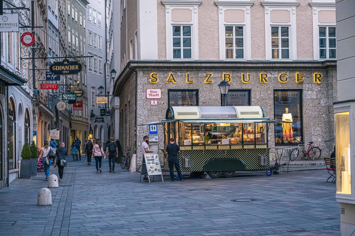 Sausage and Bosna Wurstelstand kiosk on a Salzburg Altstadt paved street at dusk with shop facades behind