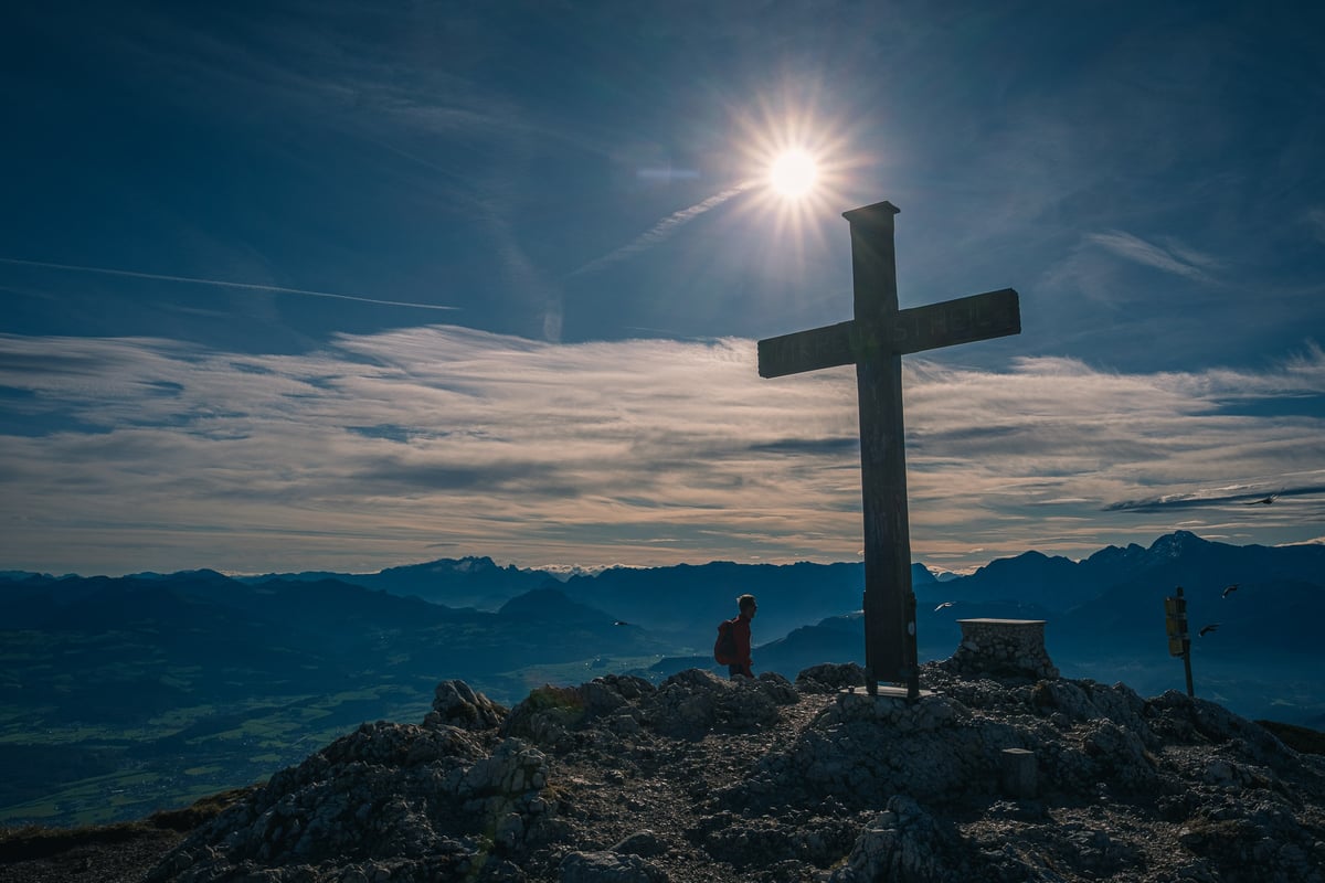 Wooden summit cross on the Berchtesgadener Hochthron backlit by bright sun over the Alps.