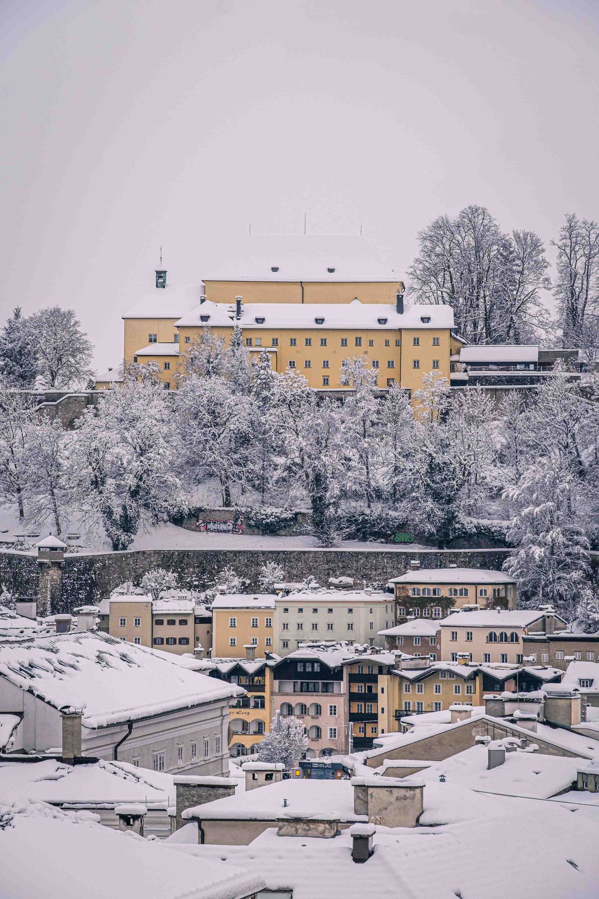 Capuchin Monastery on the Kapuzinerberg with yellow facade in fresh snow viewed from the Salzburg old town below