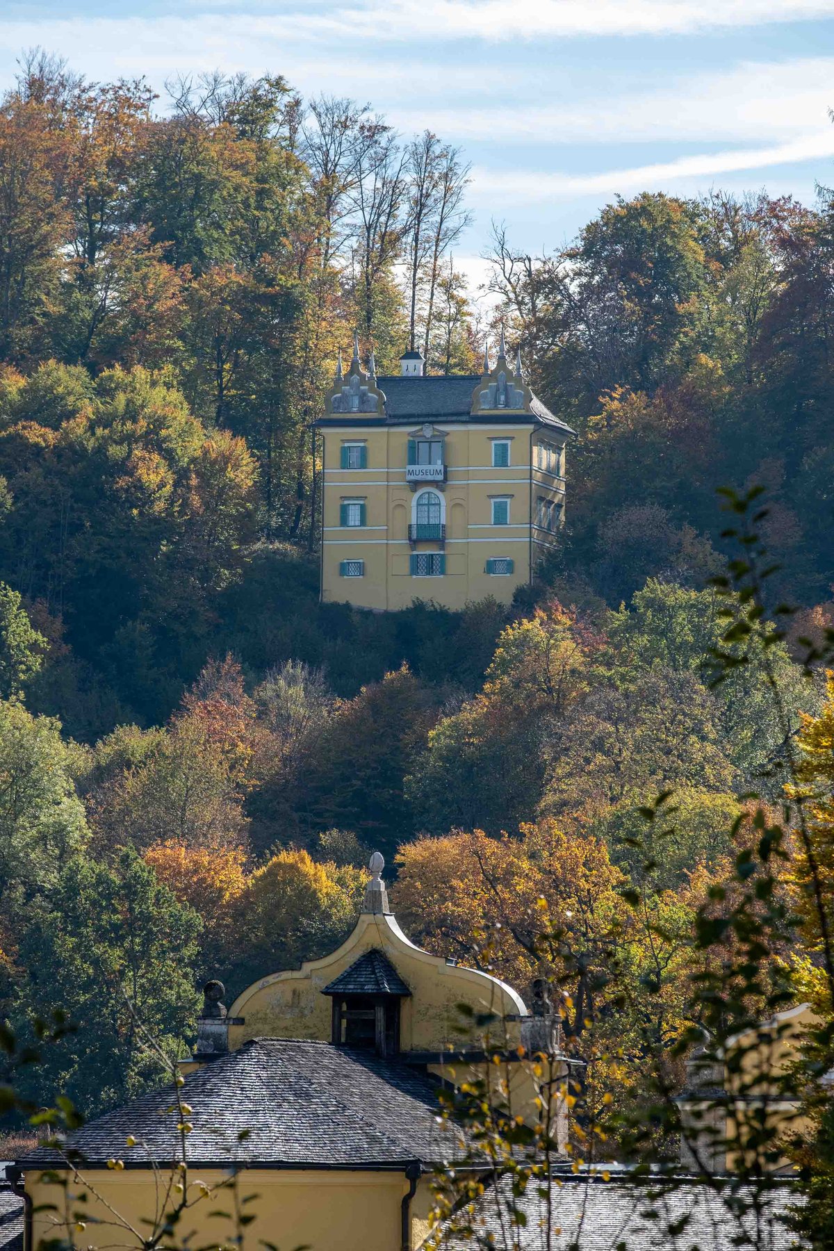 Yellow Monatsschlossl housing the Folklore Museum rising above autumn forest in Hellbrunn