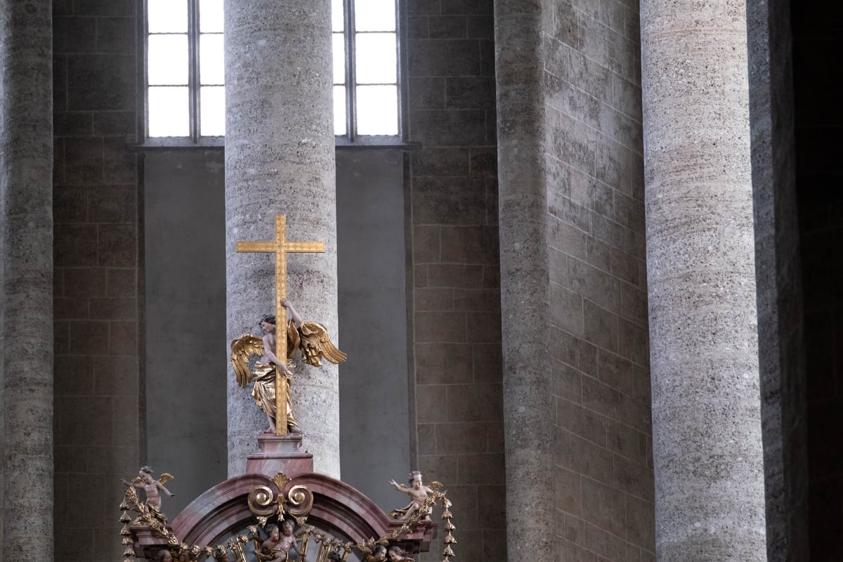 Gilded angel with golden cross above Baroque altar among stone pillars in Franziskanerkirche Salzburg
