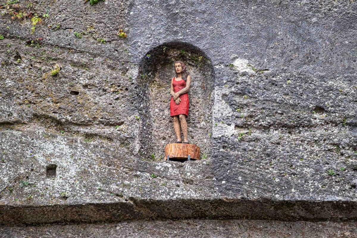 Small red-dressed sculpture set in a carved rock niche known as Frau im Fels in Salzburg