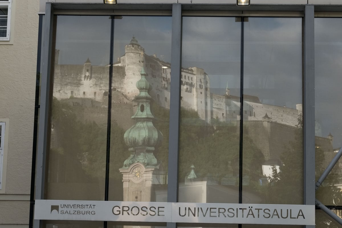 Fortress and Franciscan Church tower reflected in Grosse Universitaetsaula glass facade in Salzburg