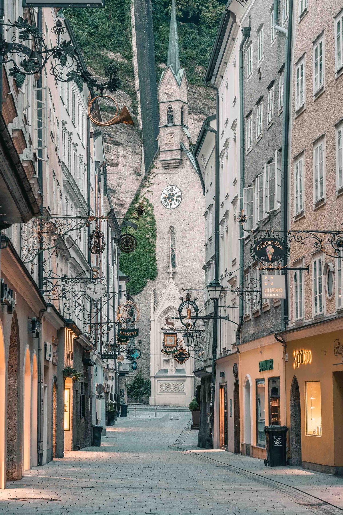 Narrow Getreidegasse with hanging guild signs leading toward Blasiuskirche tower in Salzburg