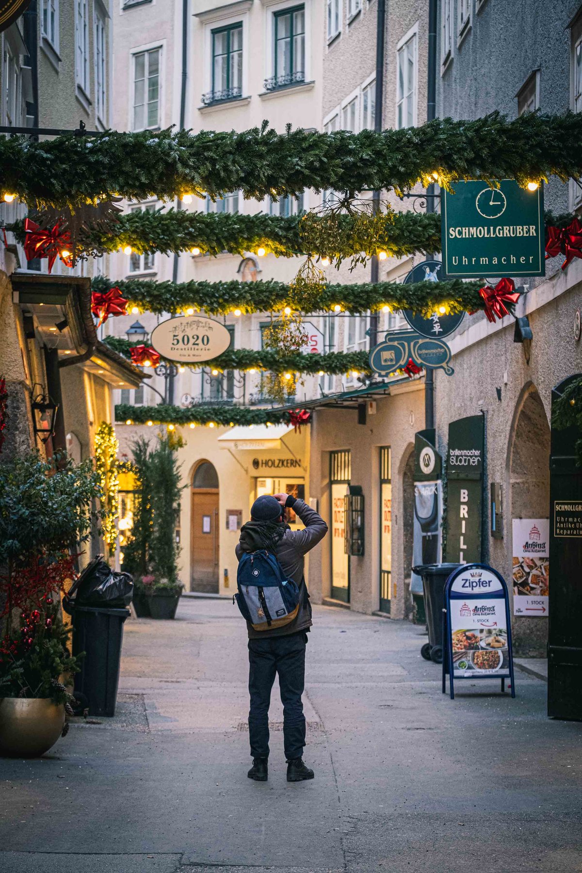 Christmas garlands and shop signs hang over Goldgasse with a photographer standing in Salzburg old town.
