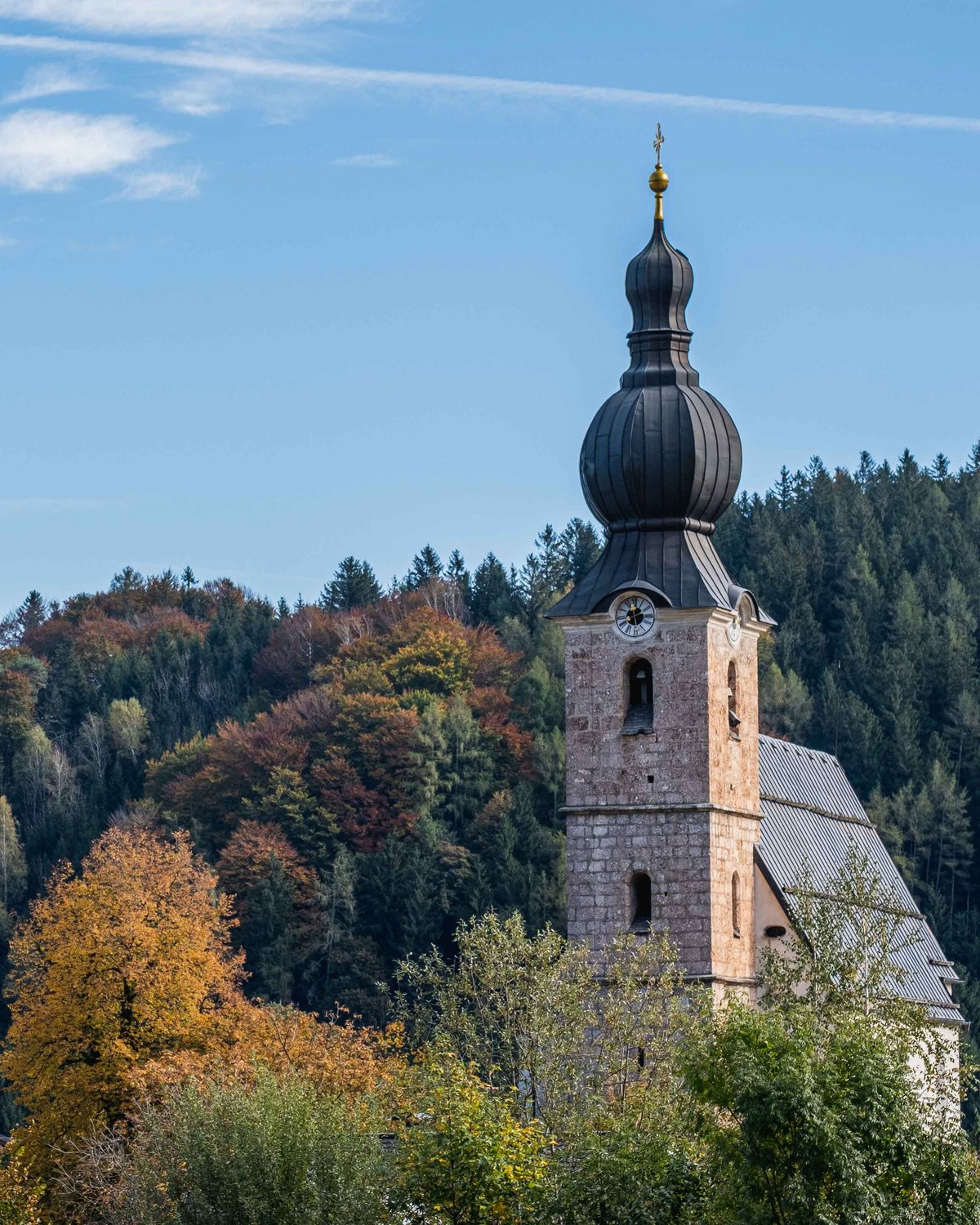 Onion-domed parish church tower rising above autumn trees in Grodig near Salzburg