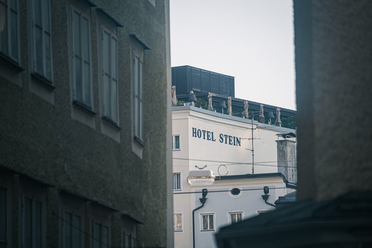 Hotel Stein signage and rooftop terrace glimpsed between Altstadt buildings across the Salzach in Salzburg.