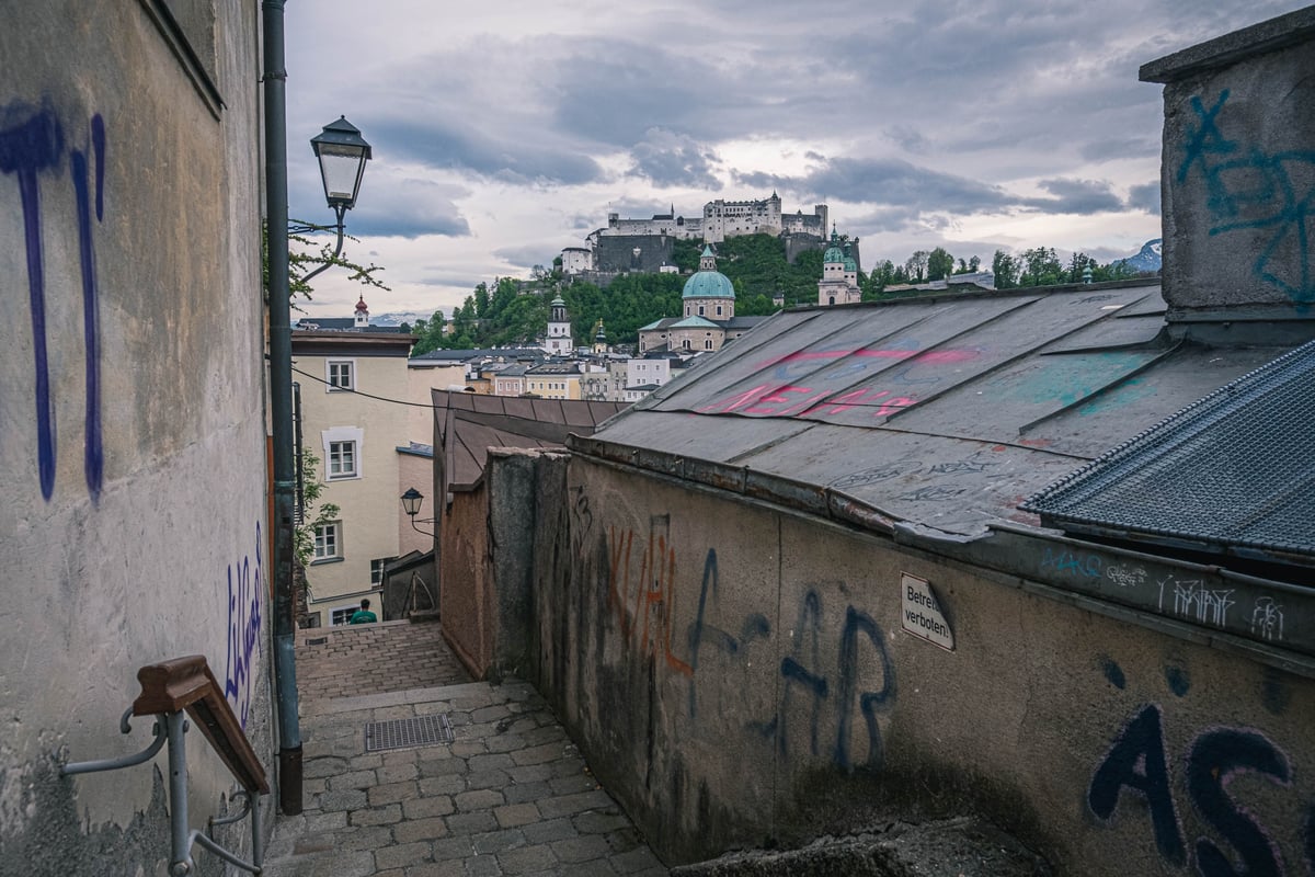 Narrow graffitied alley of the Imbergstiege with view to the Hohensalzburg Fortress on the cliff