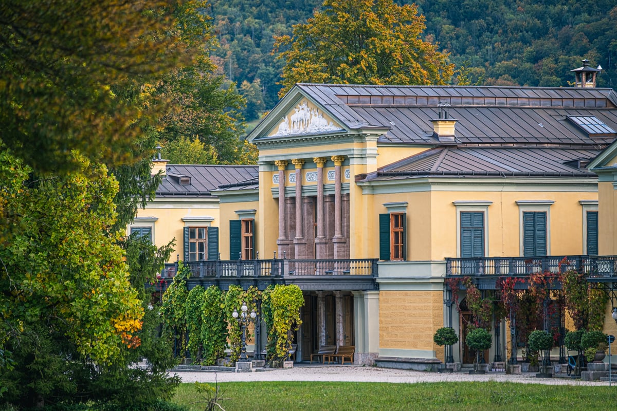 The yellow Kaiservilla in Bad Ischl seen across the park in autumn, its columned portico crowned by a white relief of deer.