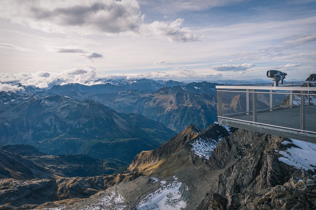 The Top of Salzburg viewing platform on the Kitzsteinhorn juts out over a rock spur with a coin telescope at its far end, above autumn valleys and range after range of peaks.