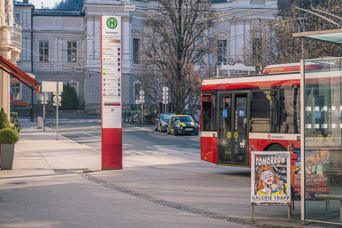 Makartplatz bus stop with red Salzburg bus passing in front of Landestheater in Salzburg.