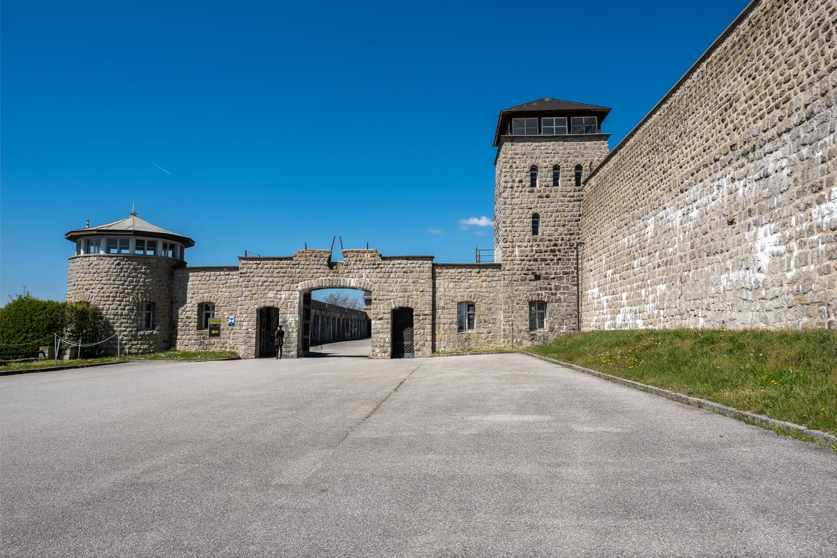 The main gate of the Mauthausen memorial photographed square on from the forecourt, with the round glazed guard tower on the left and the tall square tower on the right.
