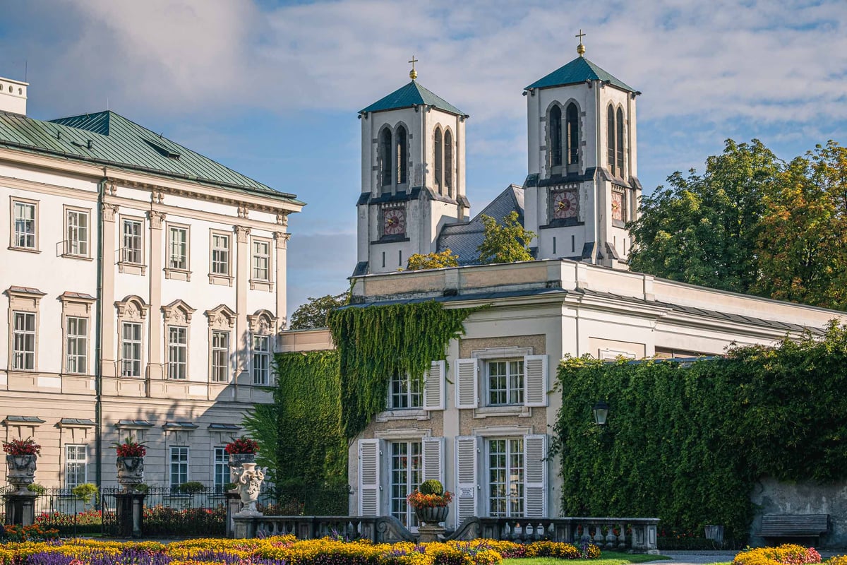 Mirabell Palace with the twin towers of Andraekirche rising behind the ivy-covered garden walls in Salzburg.
