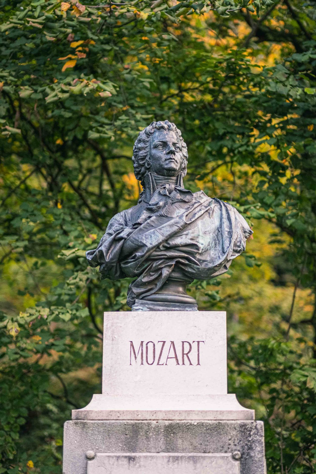Bronze Mozart bust on a stone pedestal labelled MOZART among trees on Kapuzinerberg in Salzburg.