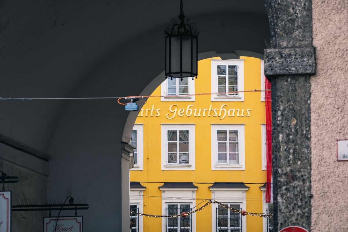 The yellow facade of Mozart's Birthplace with its Geburtshaus lettering seen through an archway in Salzburg old town.