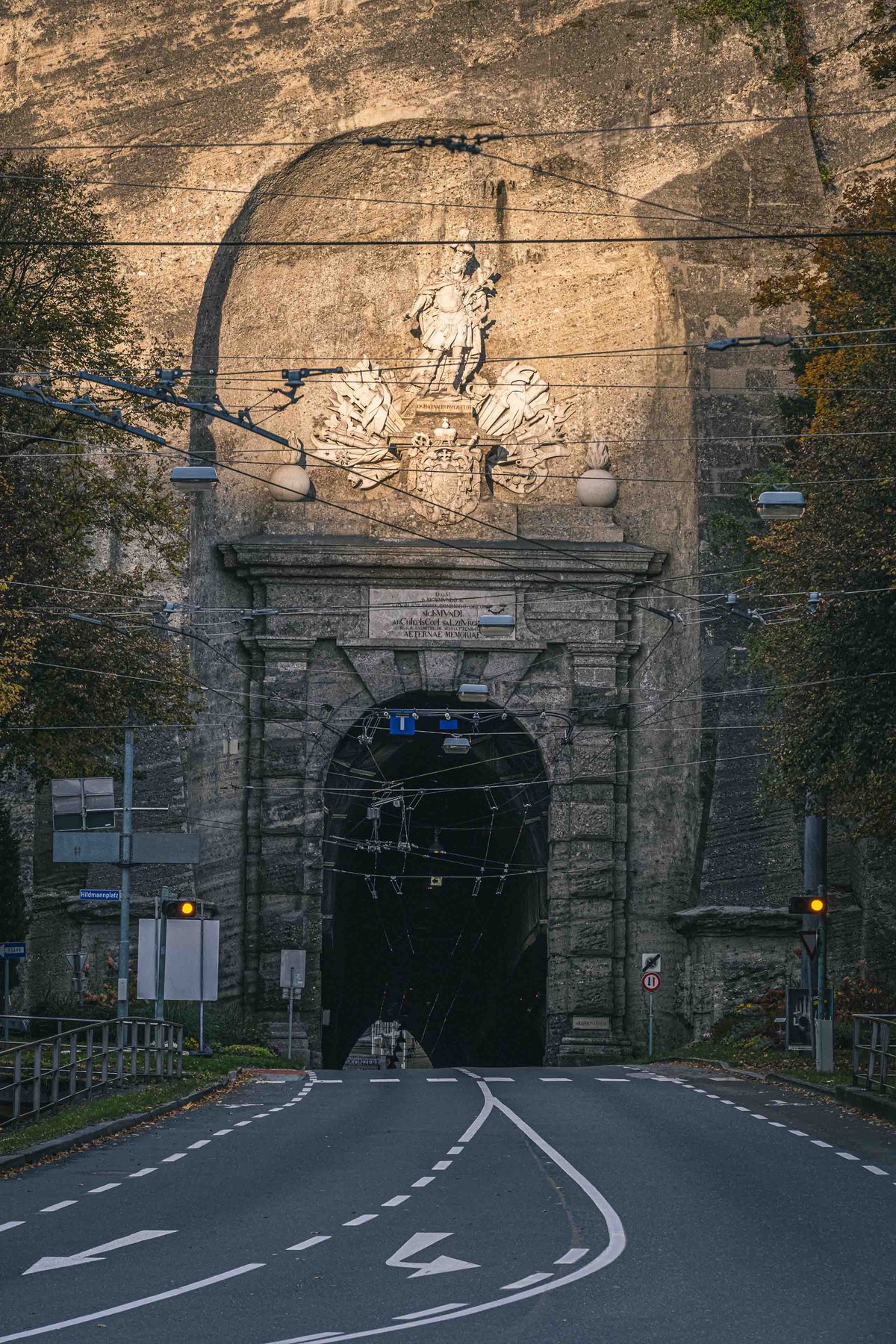 Road leading through the Neutor tunnel portal under the Monchsberg with statue relief above in Salzburg.