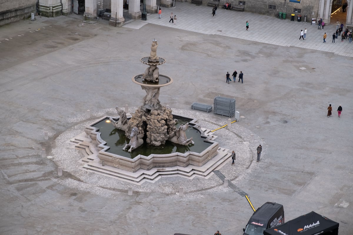 Aerial view of the baroque Residenzbrunnen with tritons and horses on the empty Residenzplatz with people walking past in Salzburg