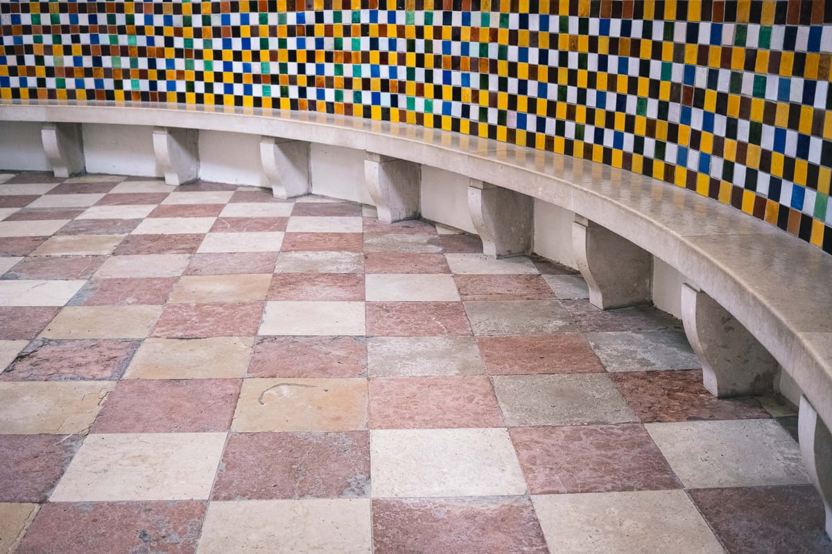 Curved bench with multicolored mosaic tile wall and checkerboard marble floor in the Gabrielskapelle (Wolf Dietrich Mausoleum) at Sebastiansfriedhof in Salzburg