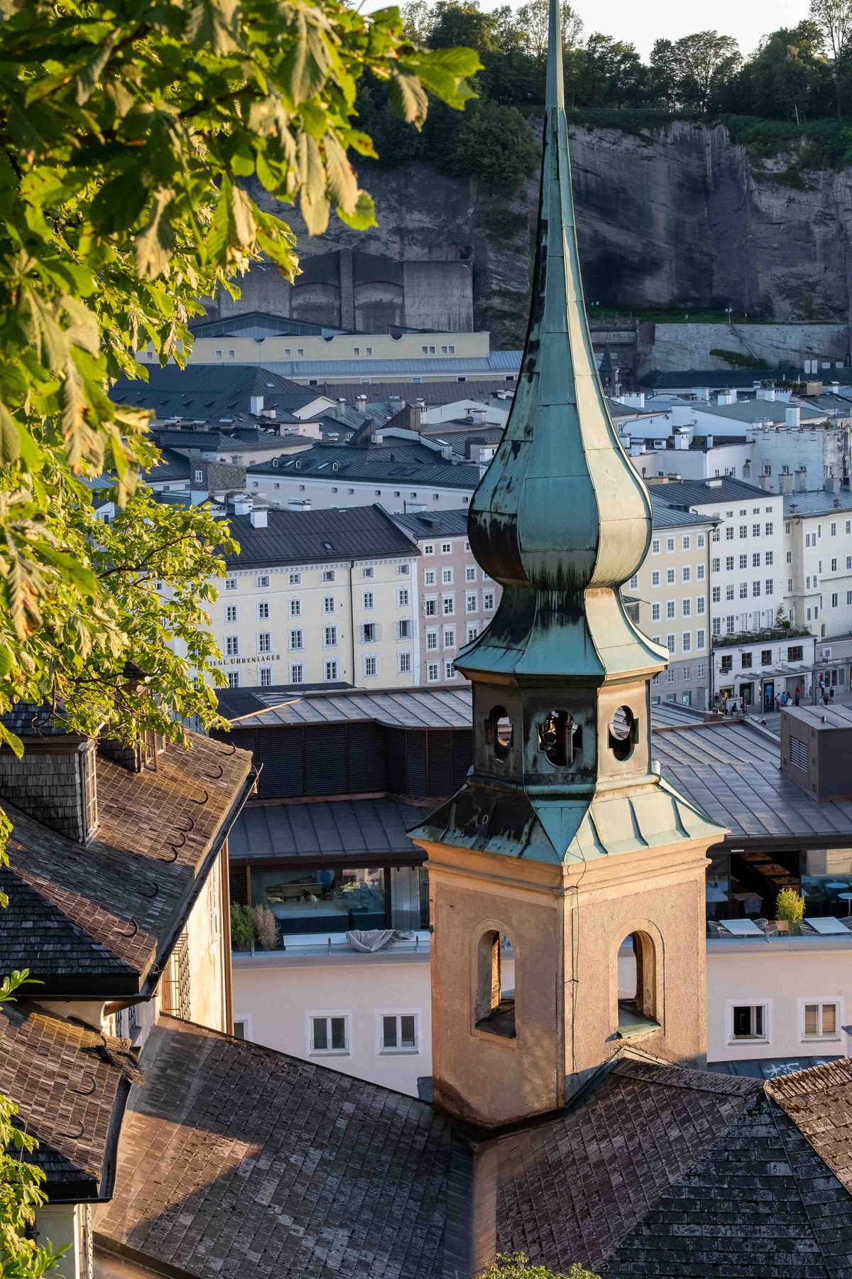 Green copper spire of the Johanneskirche at Imbergstiege rising above old town rooftops in Salzburg