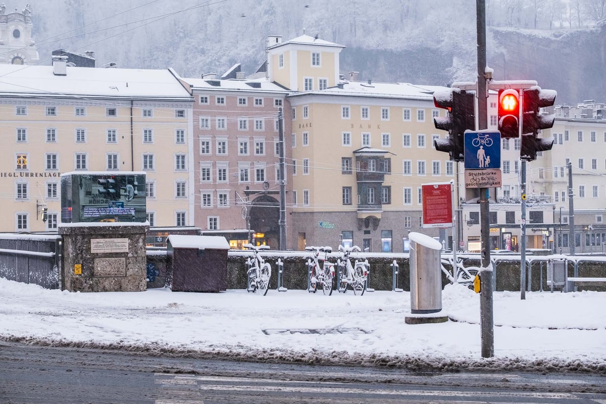 Snow-covered bikes on the Staatsbruecke railing with Altstadt facades and Moenchsberg behind in Salzburg.