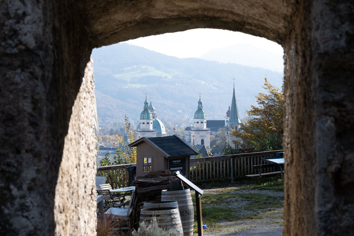 View through a stone archway at Stift St Peter showing the Salzburg Cathedral domes and mountains beyond