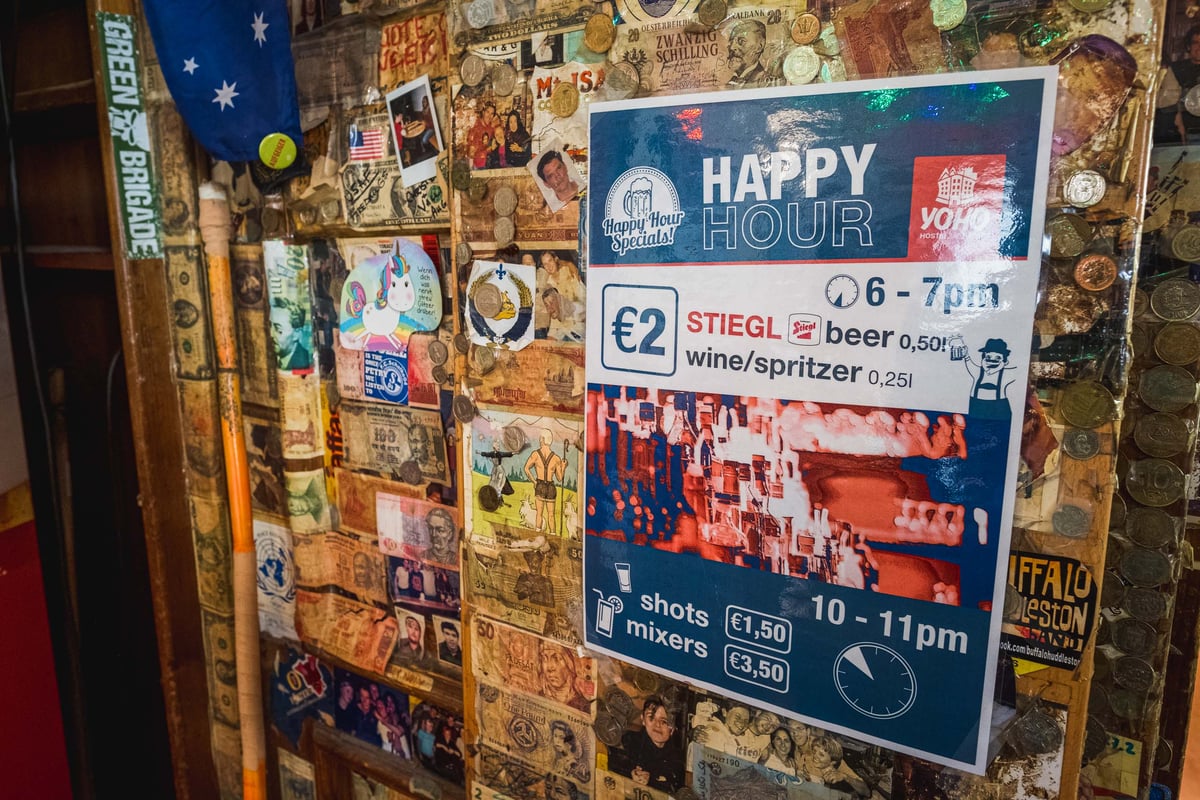 Happy hour poster on a coin covered wall inside the YoHo hostel bar in Salzburg.