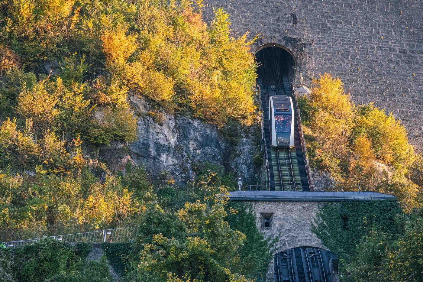 Funicular car emerging from the Festungsbahn tunnel amid autumn foliage on the fortress hillside in Salzburg.