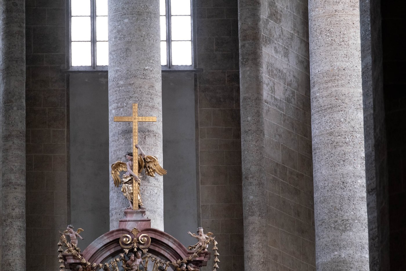 Gilded angel with golden cross above Baroque altar among stone pillars in Franziskanerkirche Salzburg