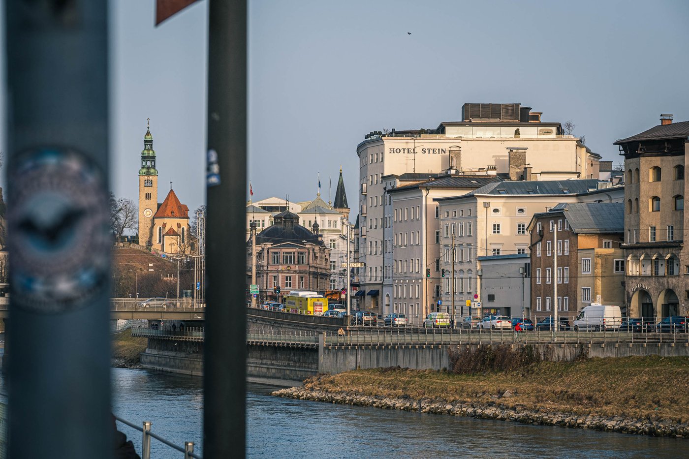 Hotel Stein and Neustadt buildings along the Salzach with a church tower rising on the left in Salzburg.