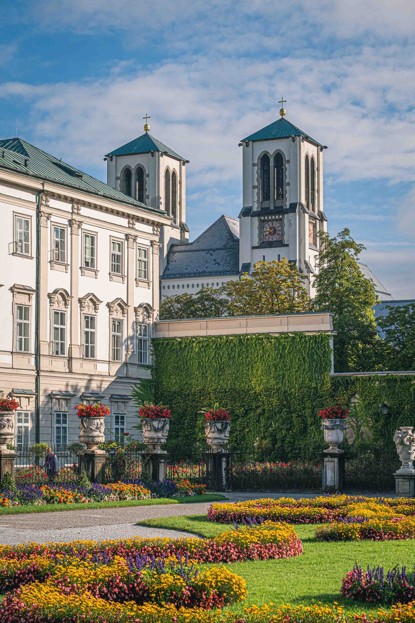 Colourful flower beds in the Mirabell Gardens with Andraekirche twin towers rising behind the ivy walls in Salzburg.