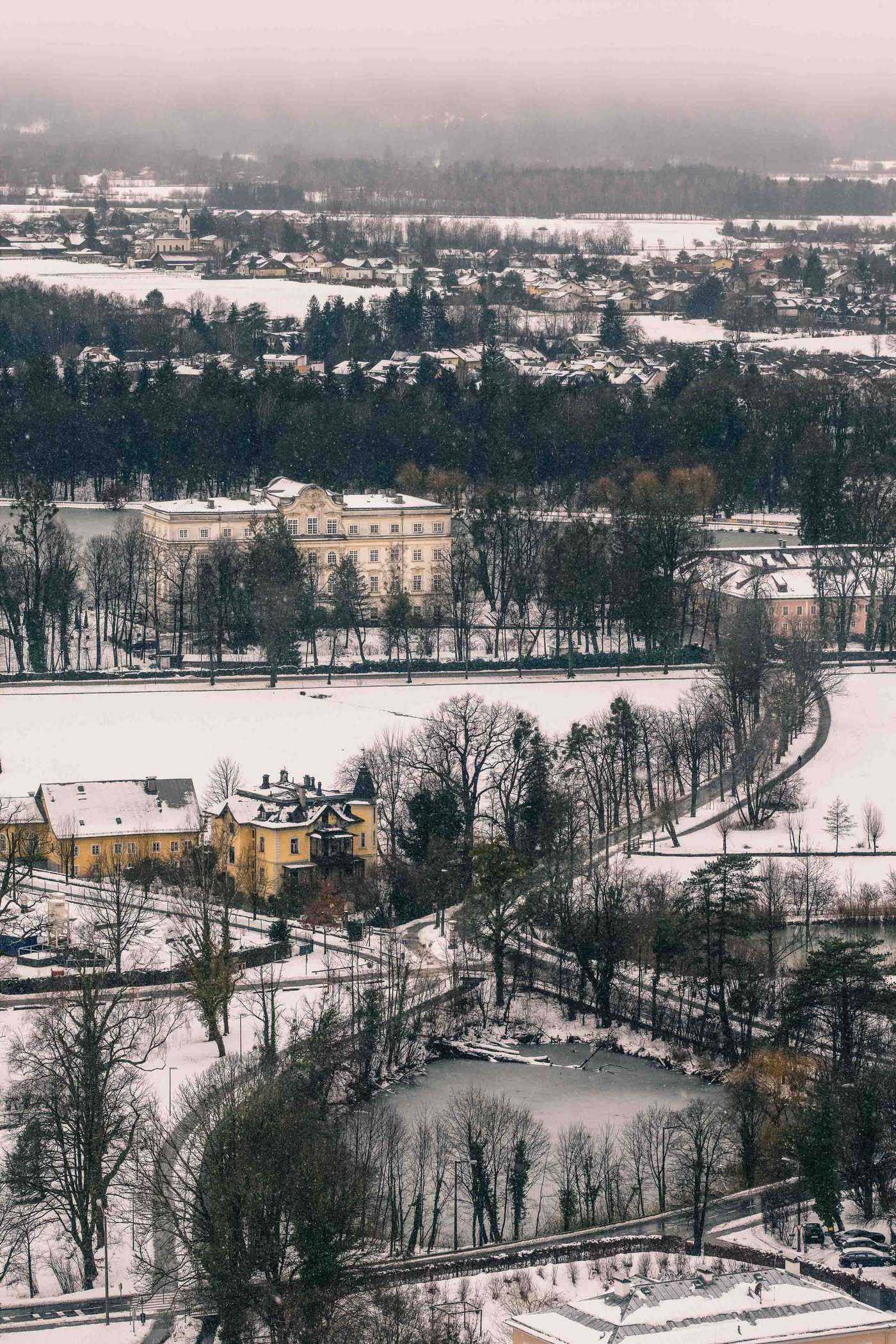 Snow covered Schloss Leopoldskron and its grounds seen from Hohensalzburg Fortress in winter.