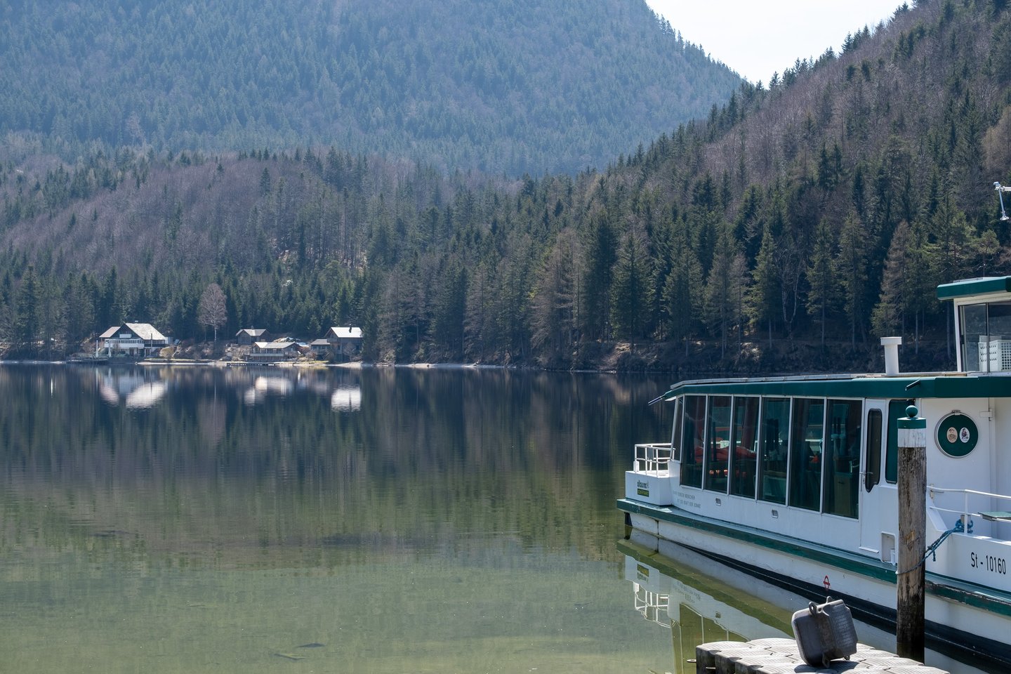 The moored excursion boat sits at the right edge of a calm view across the Altausseer See to lakeside villas under a steep forested slope.