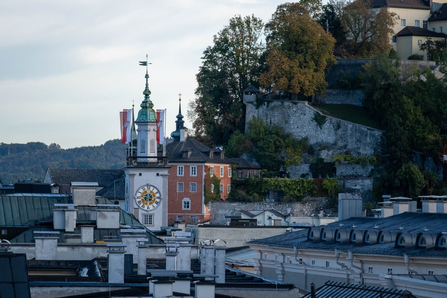 Altes Rathaus clock tower above old town rooftops with the Moenchsberg cliff rising behind in Salzburg.