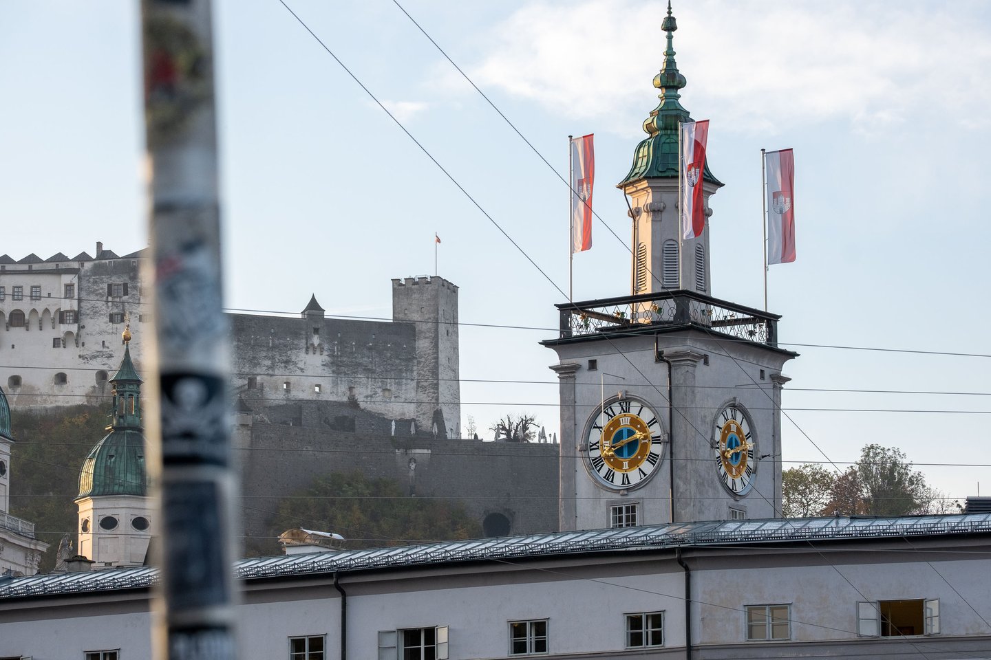 Onion-dome clock tower of the Altes Rathaus Salzburg with hung Salzburg flags and Hohensalzburg Fortress visible behind