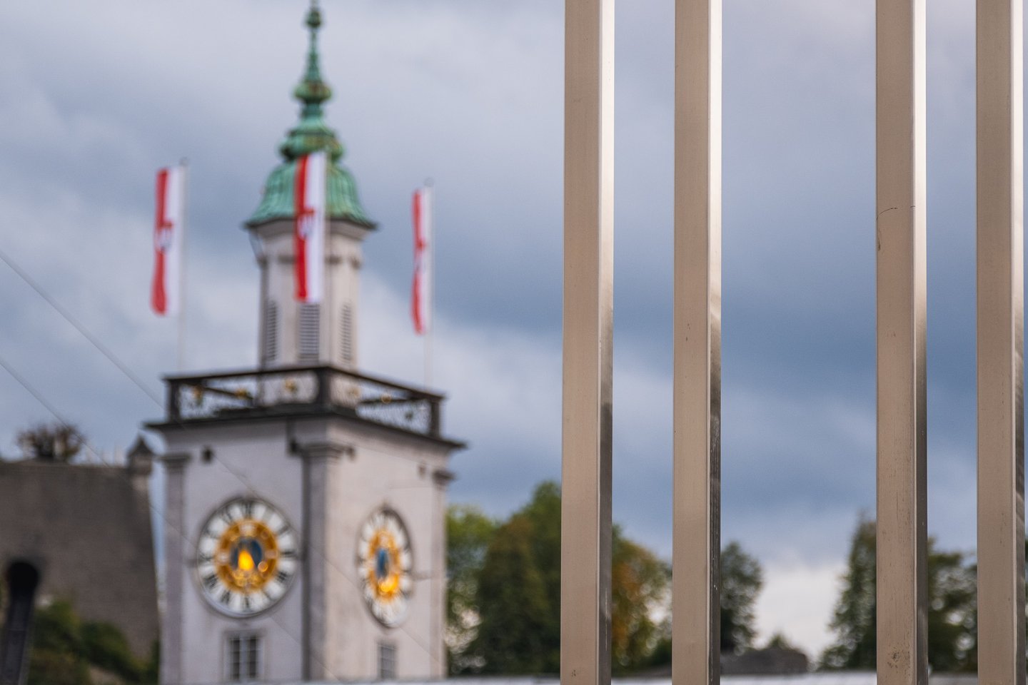 The Altes Rathaus Salzburg clock tower with green spire and red-white Austrian flags seen through a metal fence