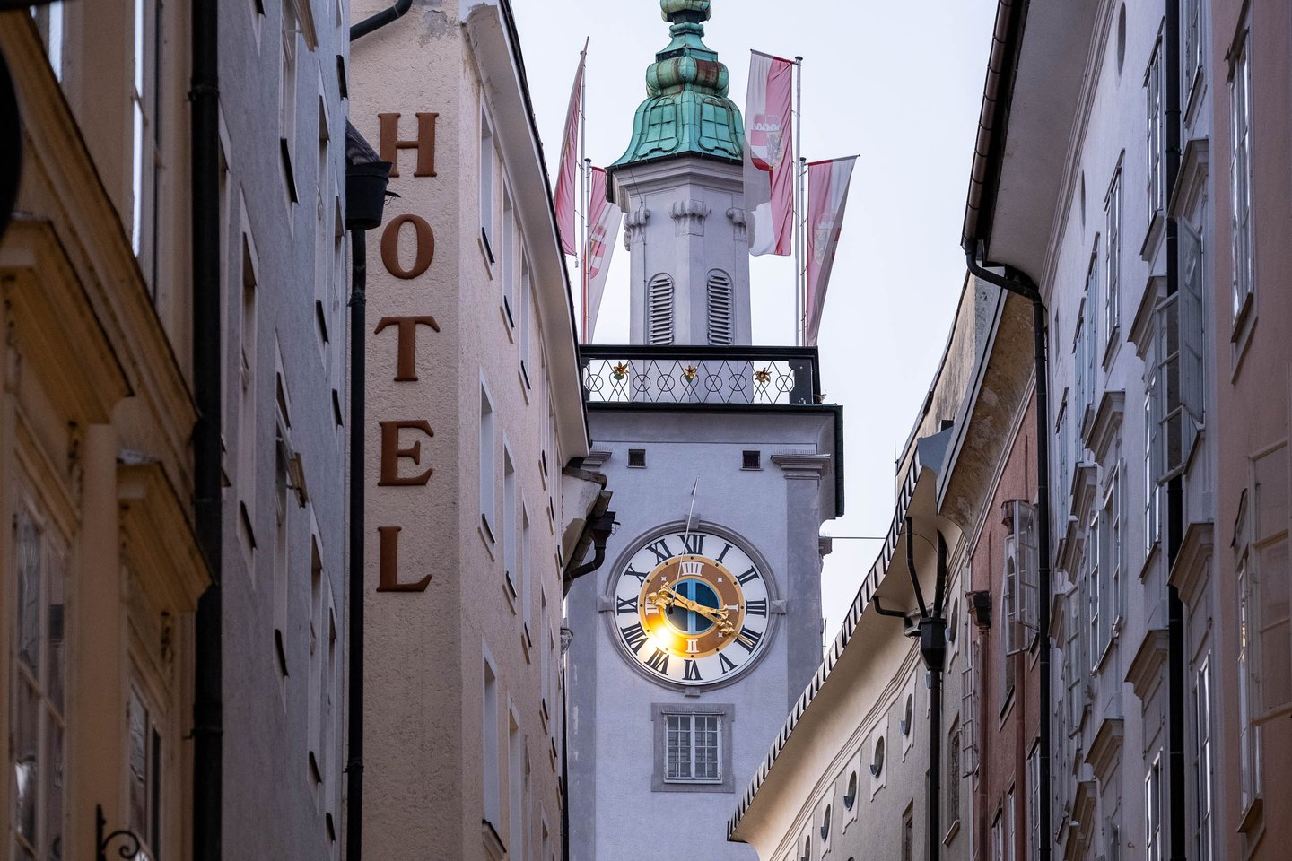 Altes Rathaus clock tower framed between narrow lanes with Hotel sign in Salzburg old town