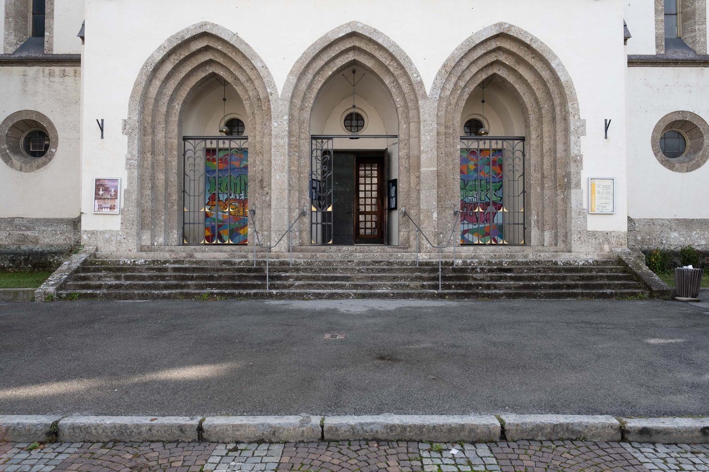 Three pointed arches frame the entrance of Andraekirche with stained glass visible in Salzburg.