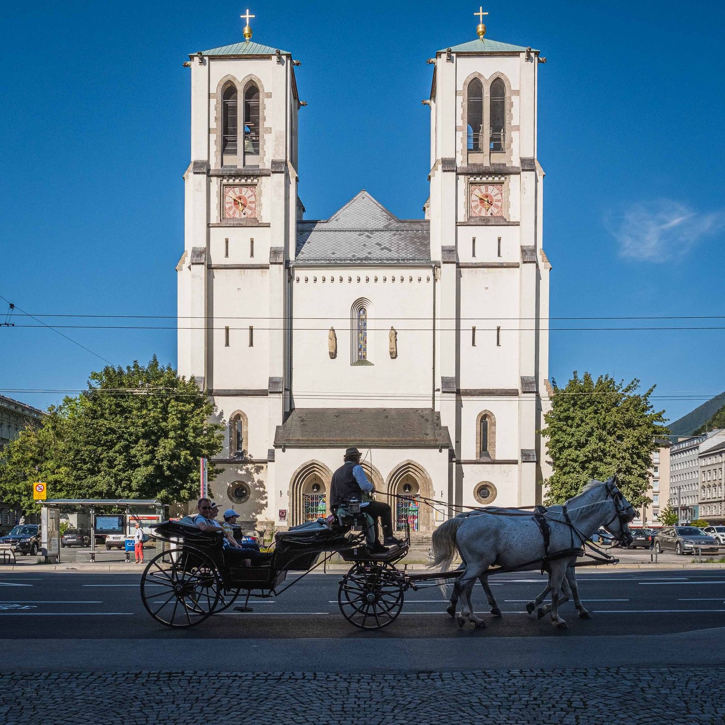 Horse drawn fiaker carriage passing Andrakirche twin towers on Mirabellplatz in Salzburg.