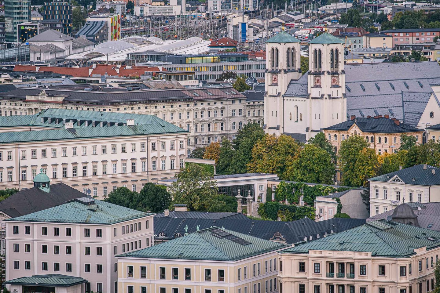 Twin-towered Andrakirche stands above Mirabell quarter rooftops with Hauptbahnhof beyond in Salzburg.