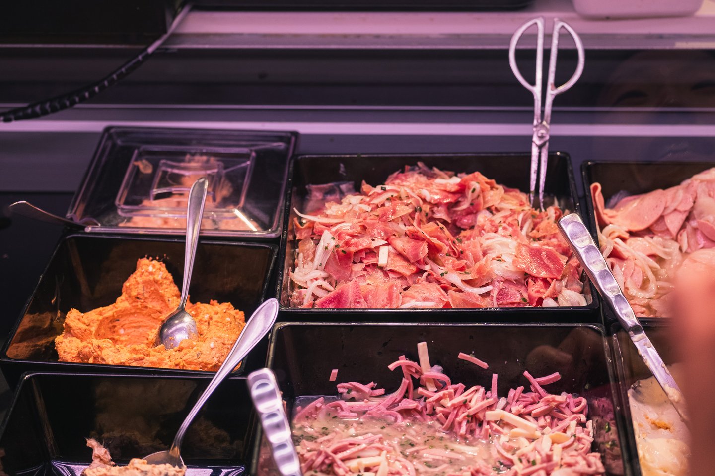 Chilled trays of Speckfleischsalat, sliced sausage salad and a paprika spread wait behind the glass of a deli counter in the food arcade of the Augustiner Braustubl in Salzburg.