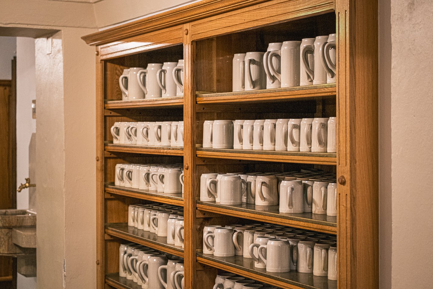 Hundreds of grey stoneware mugs fill the tall oak cupboard beside the stone rinsing fountain where guests wash their own mug at the Augustiner Braustubl.
