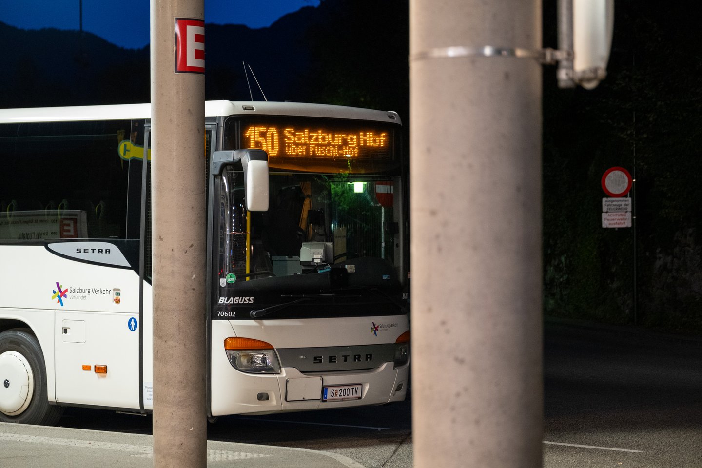 A white Setra coach in Salzburg Verkehr livery stands at Bad Ischl bus terminal after dark, its front display showing route 150 to Salzburg Hbf via Fuschl.