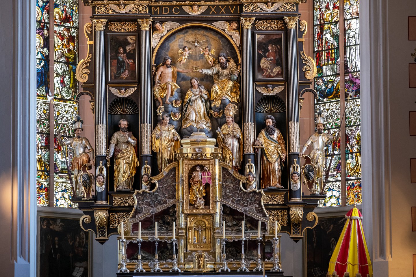 The black and gold high altar of the Mondsee basilica seen head on, with the carved Coronation of the Virgin at its centre and stained glass windows rising on either side.