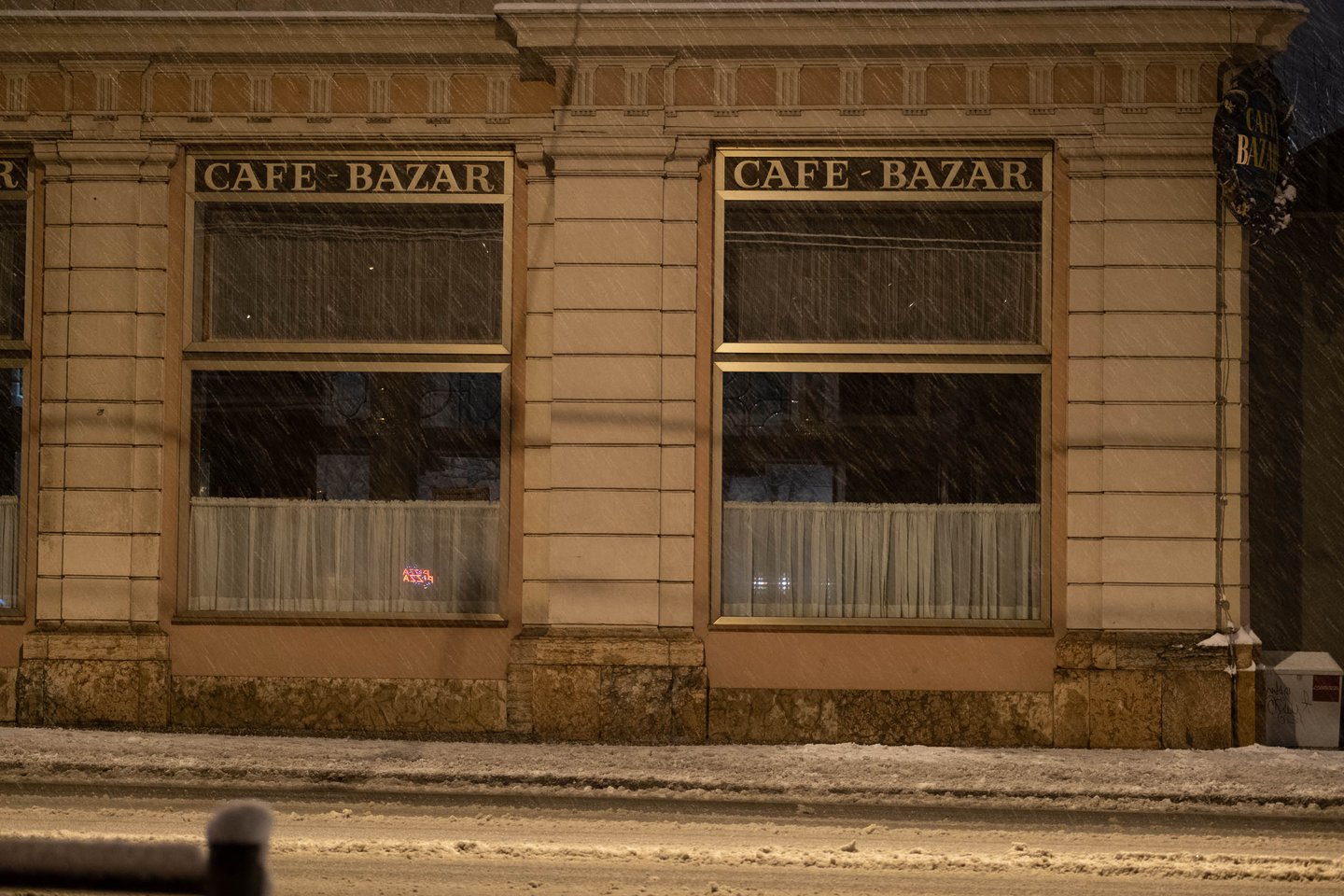 Café Bazar storefront with gold signage in heavy snowfall at night in Salzburg.