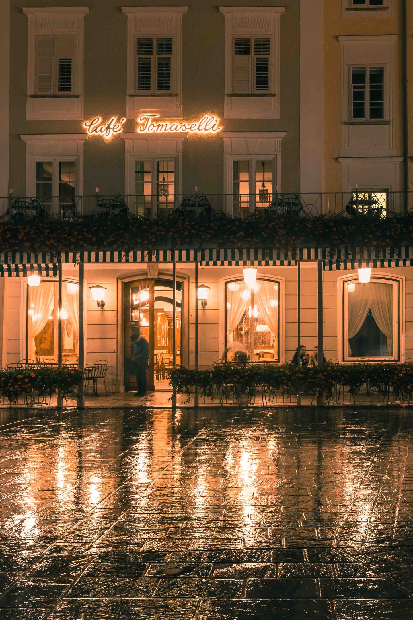 Café Tomaselli illuminated at night on Alter Markt with rain-reflected cobblestones in Salzburg