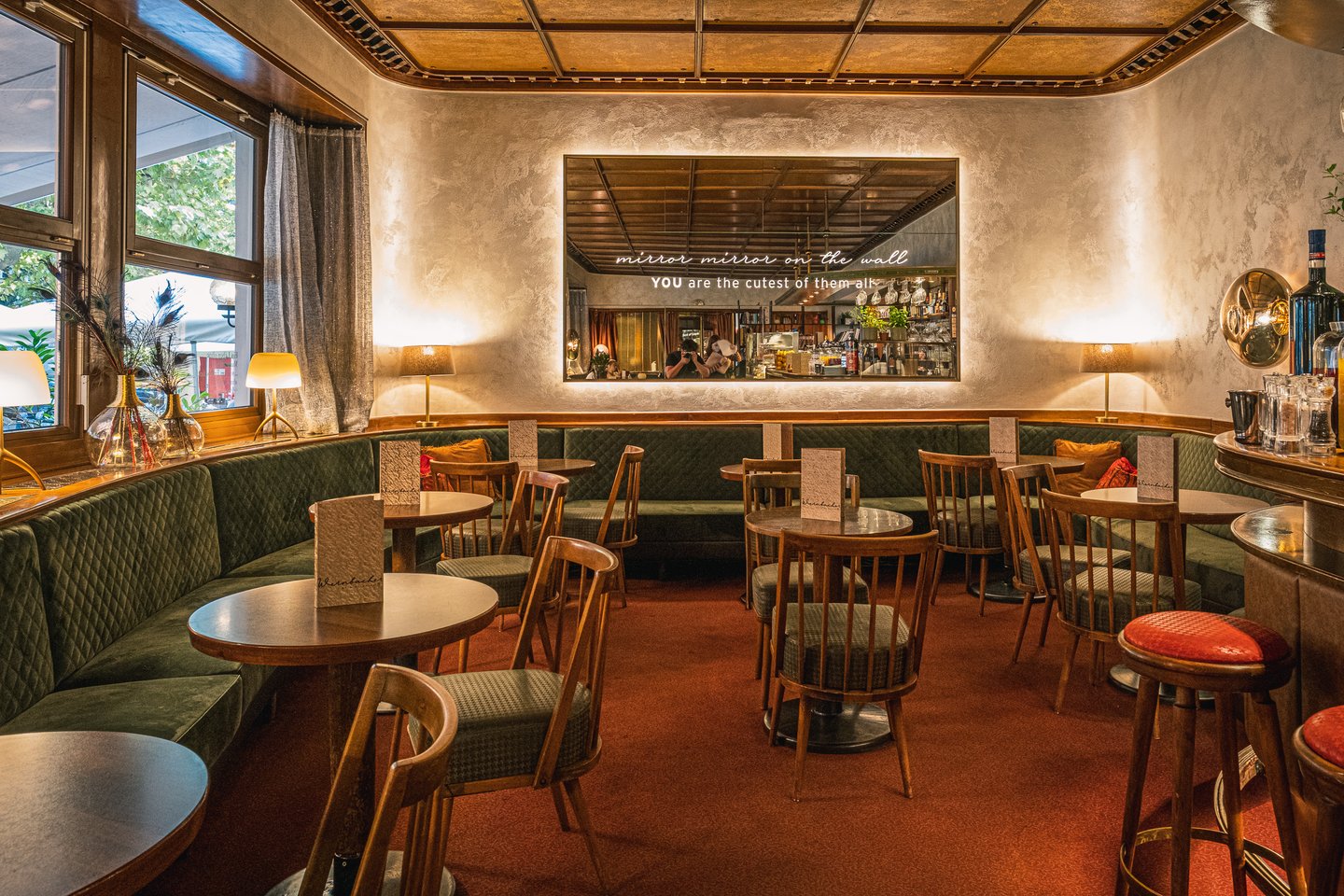 The curved green banquette, red carpet and gilded coffered ceiling of Cafe Wernbacher, with a backlit mirror lettered mirror mirror on the wall, YOU are the cutest of them all.
