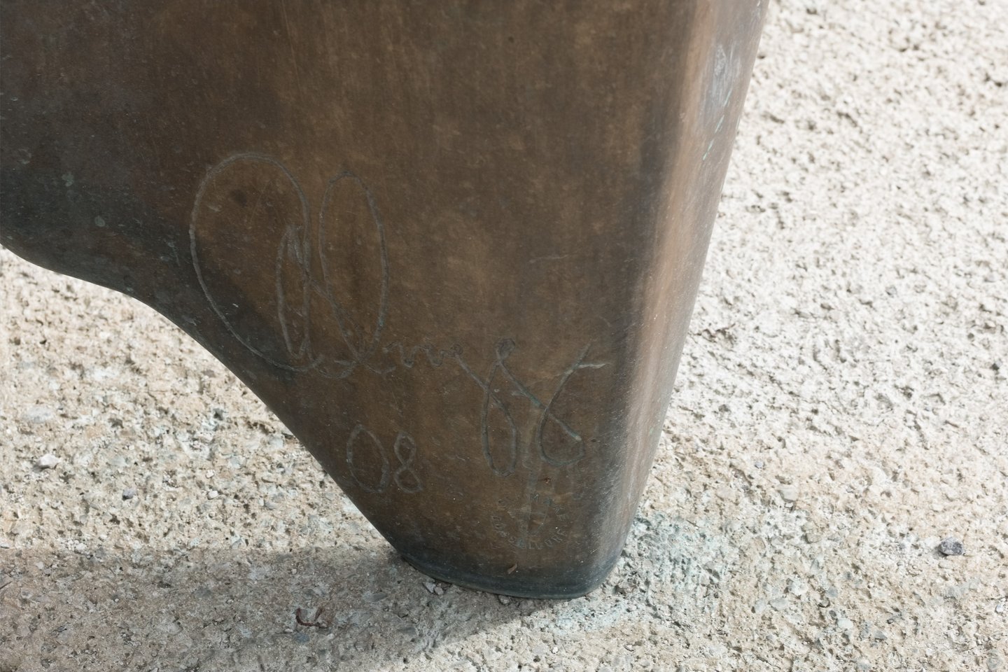 The foot of the bronze sculpture Caldera meets its concrete plinth, the metal incised with the artist's cursive signature flanked by the numerals of the year above a small foundry stamp.