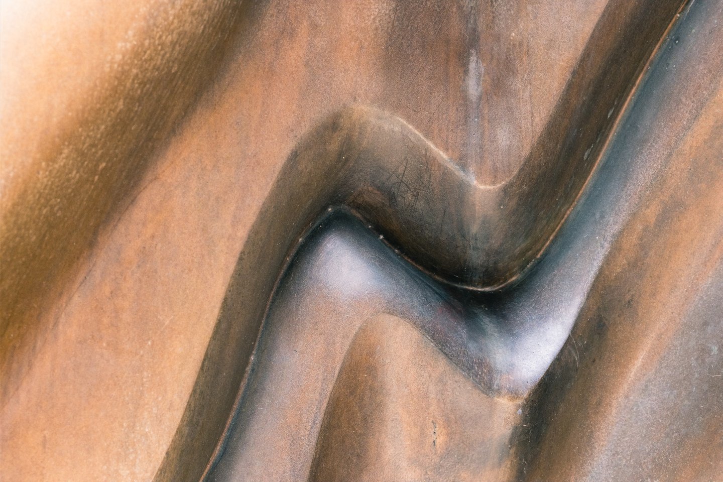 A close study of Caldera's rust-brown patina where a single rounded ridge sweeps down and doubles back on itself, the polished curve catching a cool highlight.